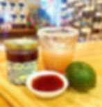Jar of jam with a small bowl filled with strawberry margarita jam, a lime, and a margarita in a cocktail glass in background