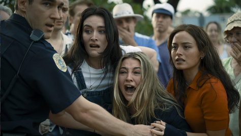 A group of girls screaming as a cop holds them back