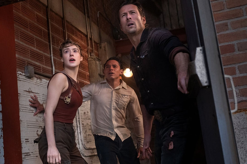 A woman and two men in a doorway look on in horror at something we can't see