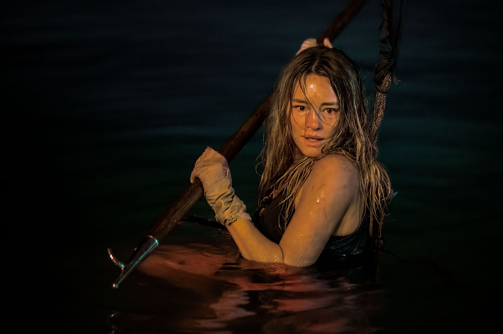 Woman in dark water holds pole, wearing gloves. Her expression is intense. The dim lighting creates a dramatic mood.
