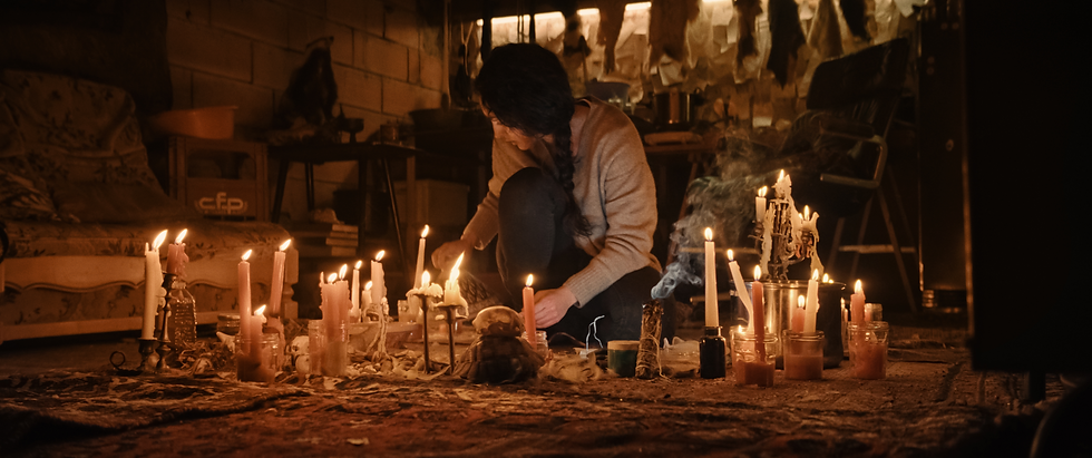 A person arranges candles in a dimly lit room. Lit candles create warm glow, smoke trails visible. Cozy and mysterious atmosphere.
