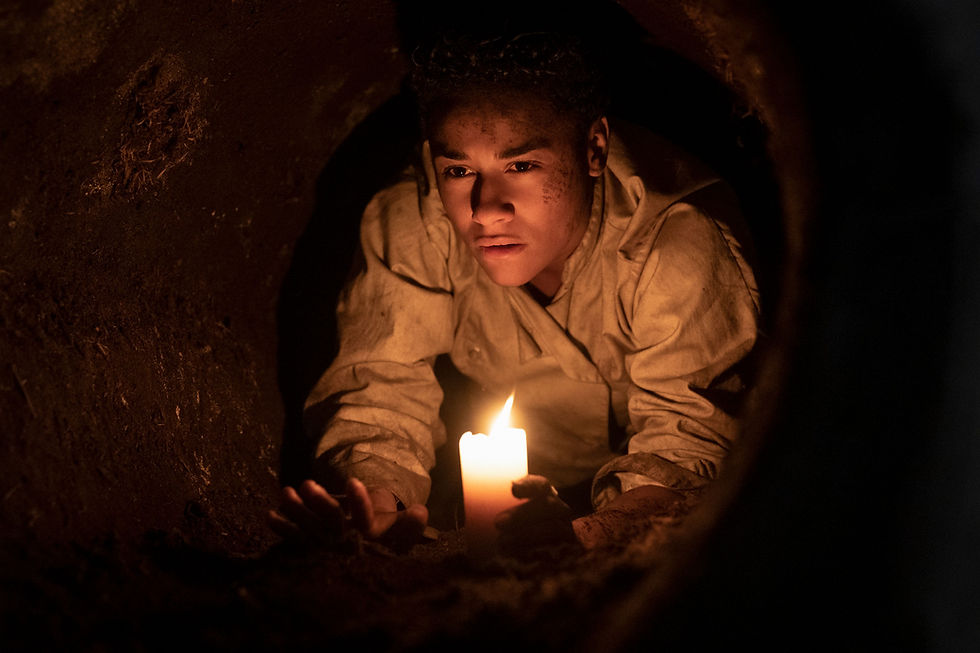A woman crawls through a dirt tunnel with a candle in her hand
