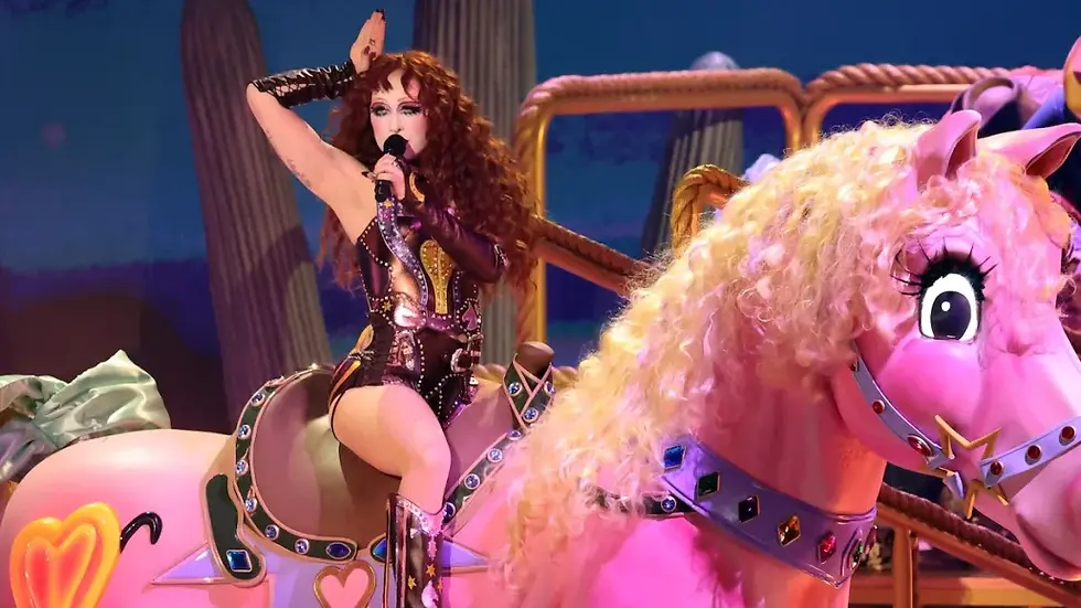 Performing artist with curly hair sings on stage, sitting on a large pink toy horse with a jeweled harness. Vibrant and theatrical scene.