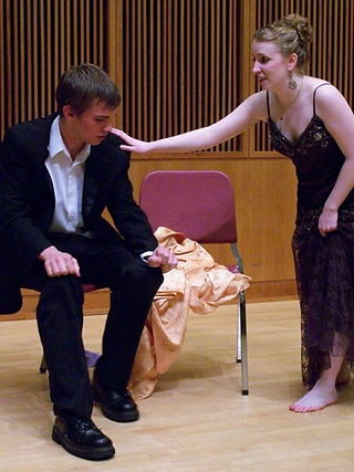 girl in purple gown places hand in concern on boy in tux seated on a chair