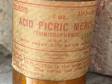 Close-up of an old amber poison bottle label reading ACID PICRIC MERCURY (TRINITROPHENOL), with faded red text.