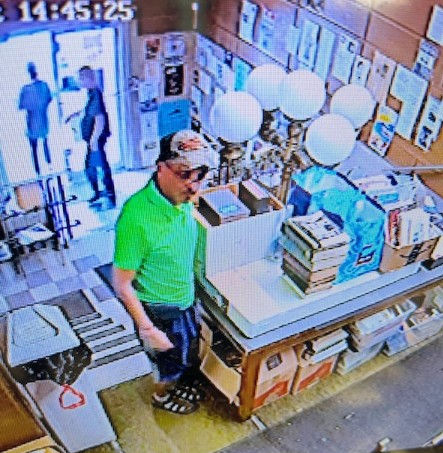 CCTV view of a man in a green polo and cap by a bookstore counter with balloons; two people stand at the entrance, 14:45:25.