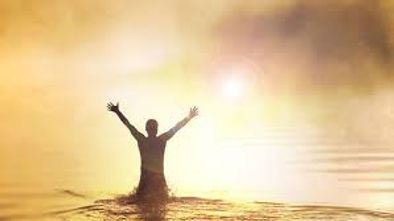Person standing in water with raised hands, symbolizing being born again through faith in Jesus Christ and receiving new spiritual life.