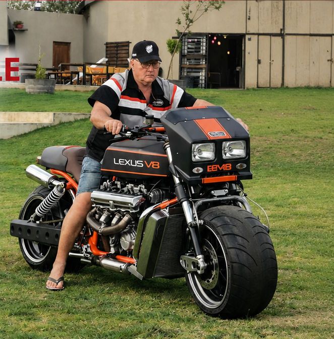 A custom V8 motorcycle standing on grass; the rider is the builder of the bike