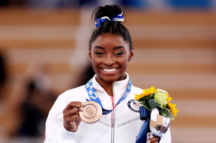 Simone Biles holding a gold medal at the olympics, (Photo by Jamie Squire. Getty Images)
