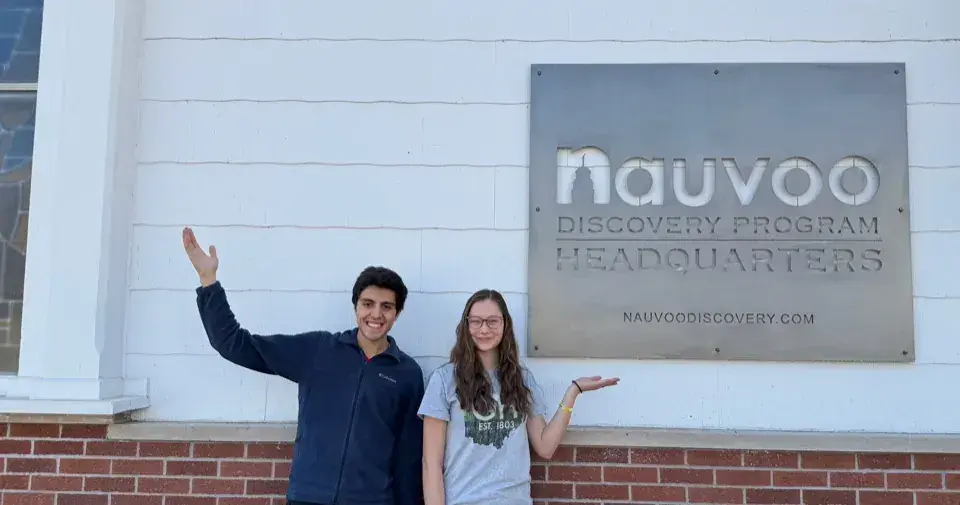 Two students pose in front of the Nauvoo Discovery Program Headquarters sign