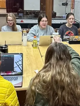 NDP students gather around a table with laptops during orientation
