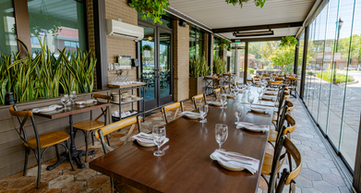 Upscale outdoor dining space under modern aluminum pergola system with rotating louvers, motorized drop screens and sliding glass panel walls.