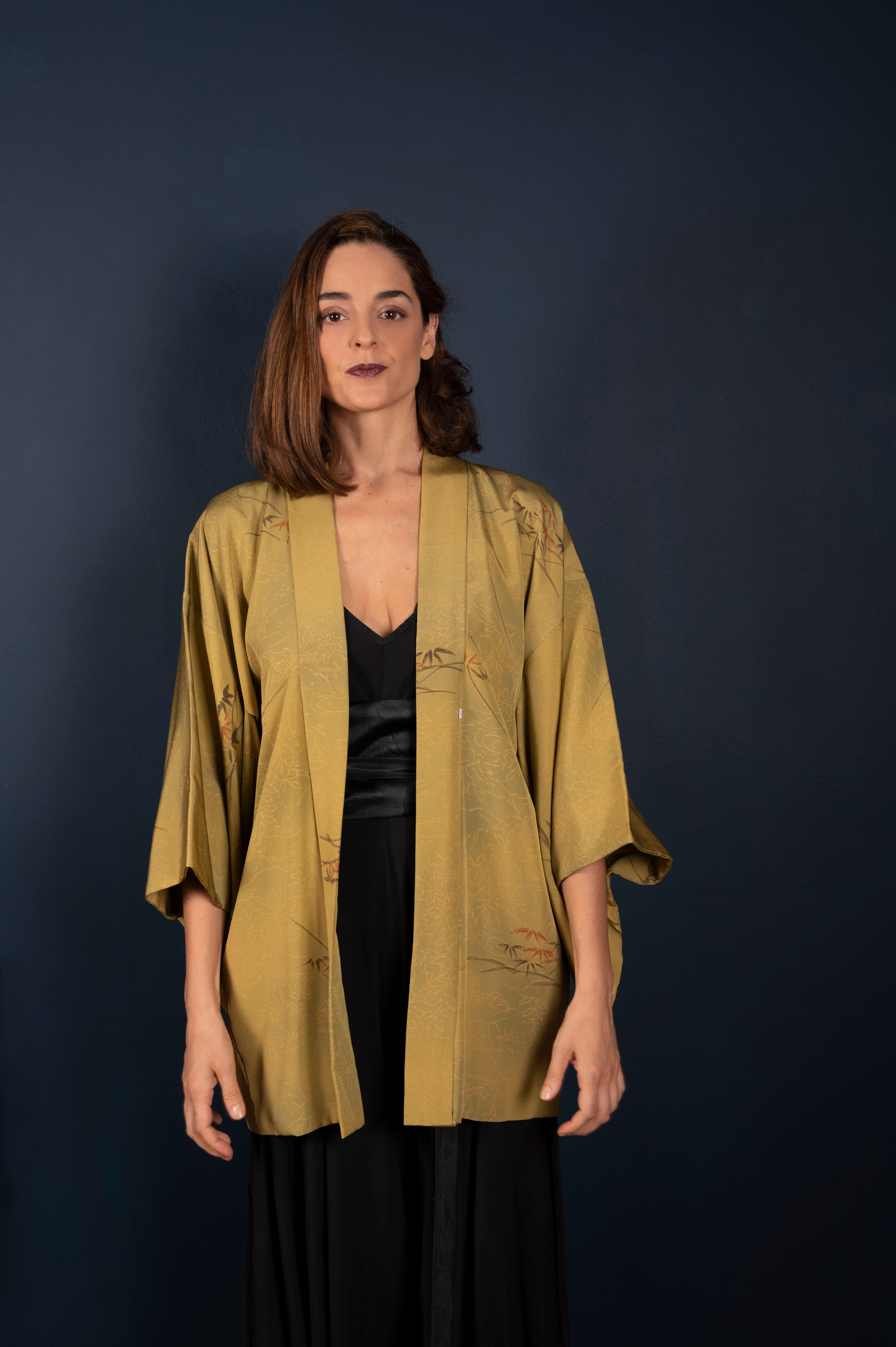 Model wearing a handmade vintage Japanese haori in olive green silk with subtle bamboo and floral motifs. The jacket is open,