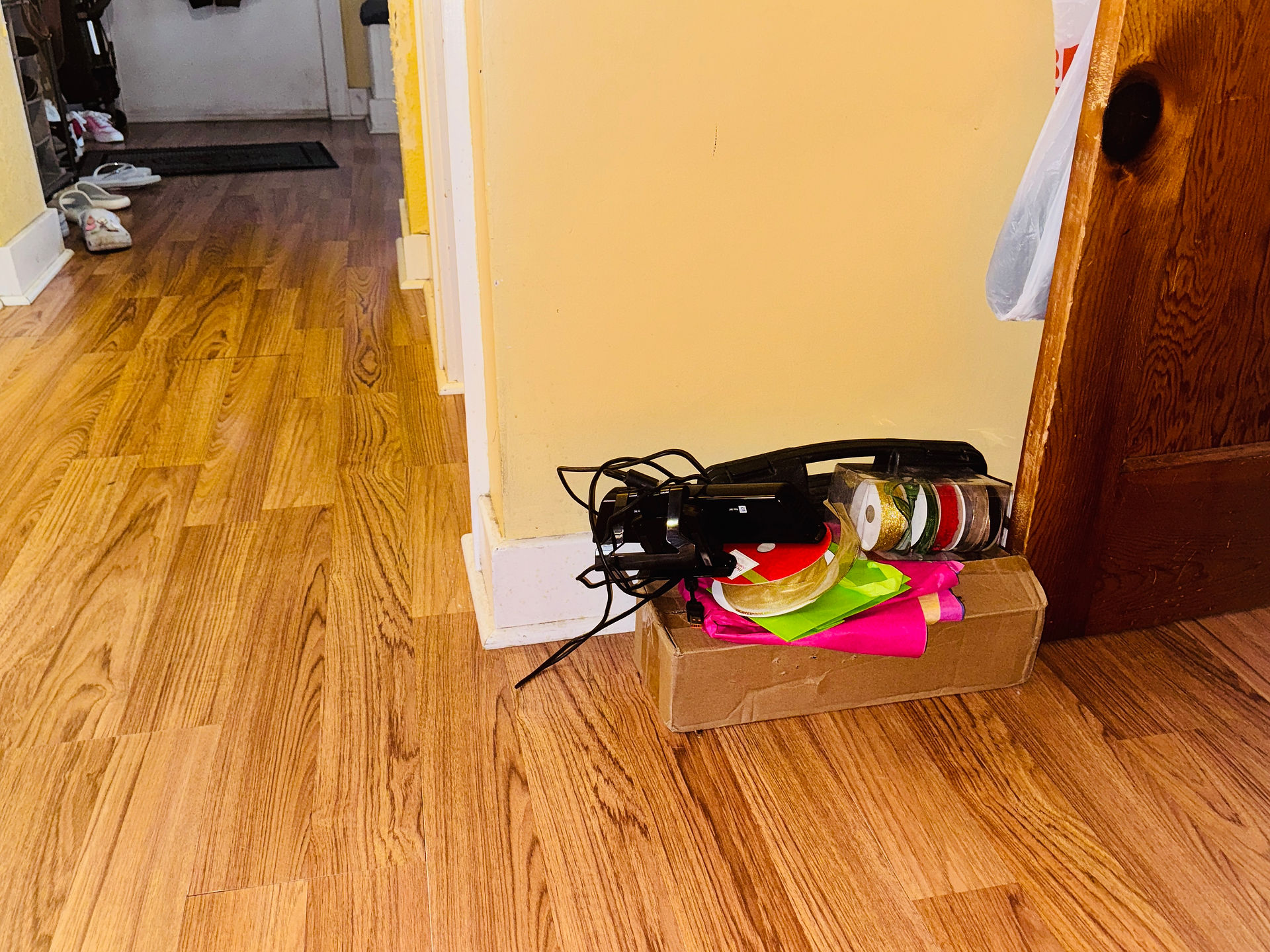 A small pile, consisting of a brown cardboard box, tissue paper for wrapping, ribbons, and a handheld machine with a wire and plug, are stacked in the hallway, next to the basement door. This is the Take Downstairs Drop Zone - where everything that belongs in the basement gets piled to get taken downstairs at some point.