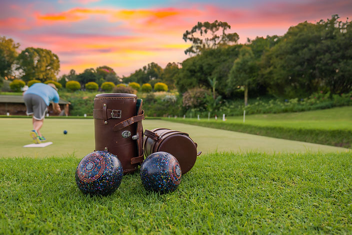 Brown leather bowls case in foreground with bowler deliverying on the green