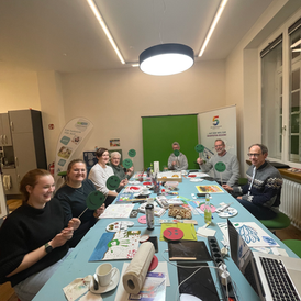 Workshopteilnehmer*innen sitzen im Raum und halten grüne Smileys nach oben, die ihre Stimmung signalisieren.