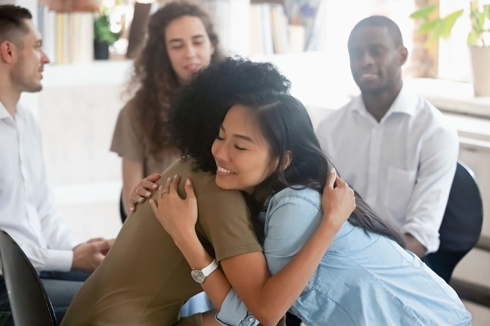 A group talking, and two women in the group giving each other a supportive hug.