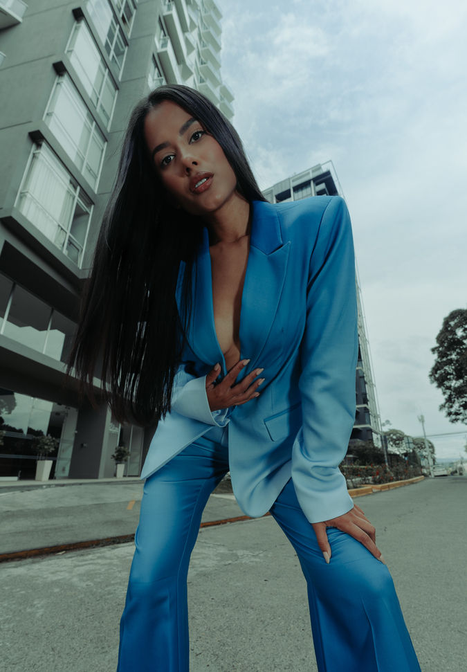 Mujer con blazer azul posando en ángulo bajo frente a edificio moderno, expresión segura y fondo urbano. Fotografía de marca personal o editorial ejecutiva por Kevin Reyes en Costa Rica