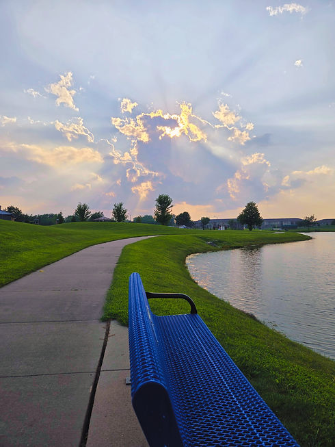 Blue bench by a lake and path under a cloudy sunset sky.