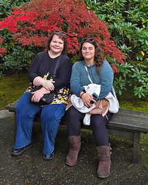 Two women smiling on a bench in front of a red maple tree.