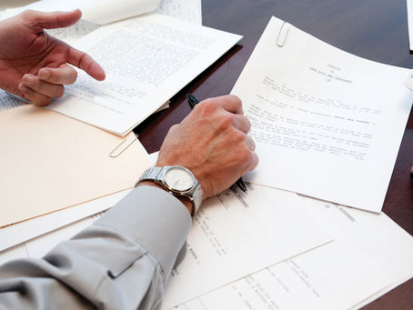 Hands reviewing legal documents on a wooden table, with a beige folder and paper clips. Focused atmosphere.