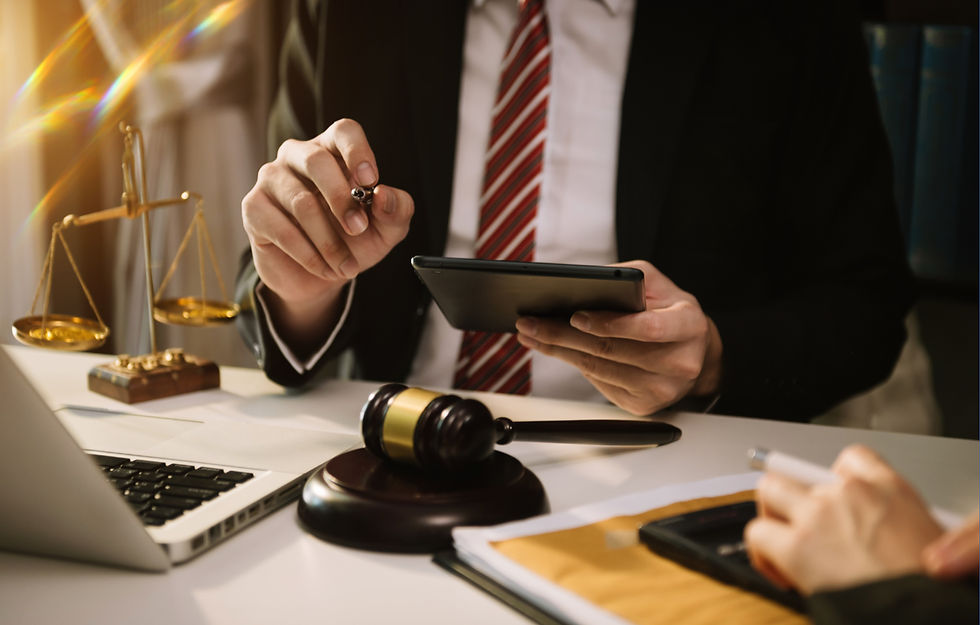 Man in suit holding tablet, sitting at a desk with gavel, scales of justice, and laptop. Professional setting, warm light, business mood.