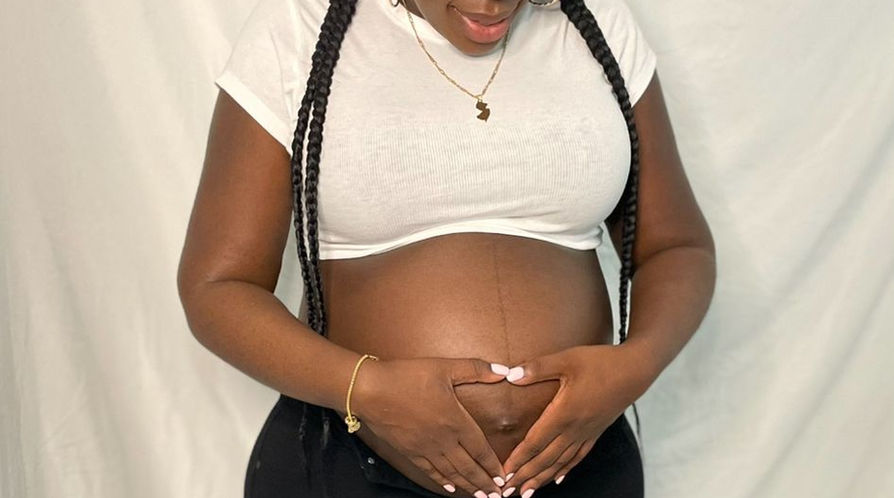 Pregnant woman in glasses and white shirt holding her baby bump.