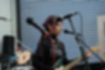 Young musician with purple hair playing electric guitar and wearing a TRACKS Sheffield t-shirt during a live performance.