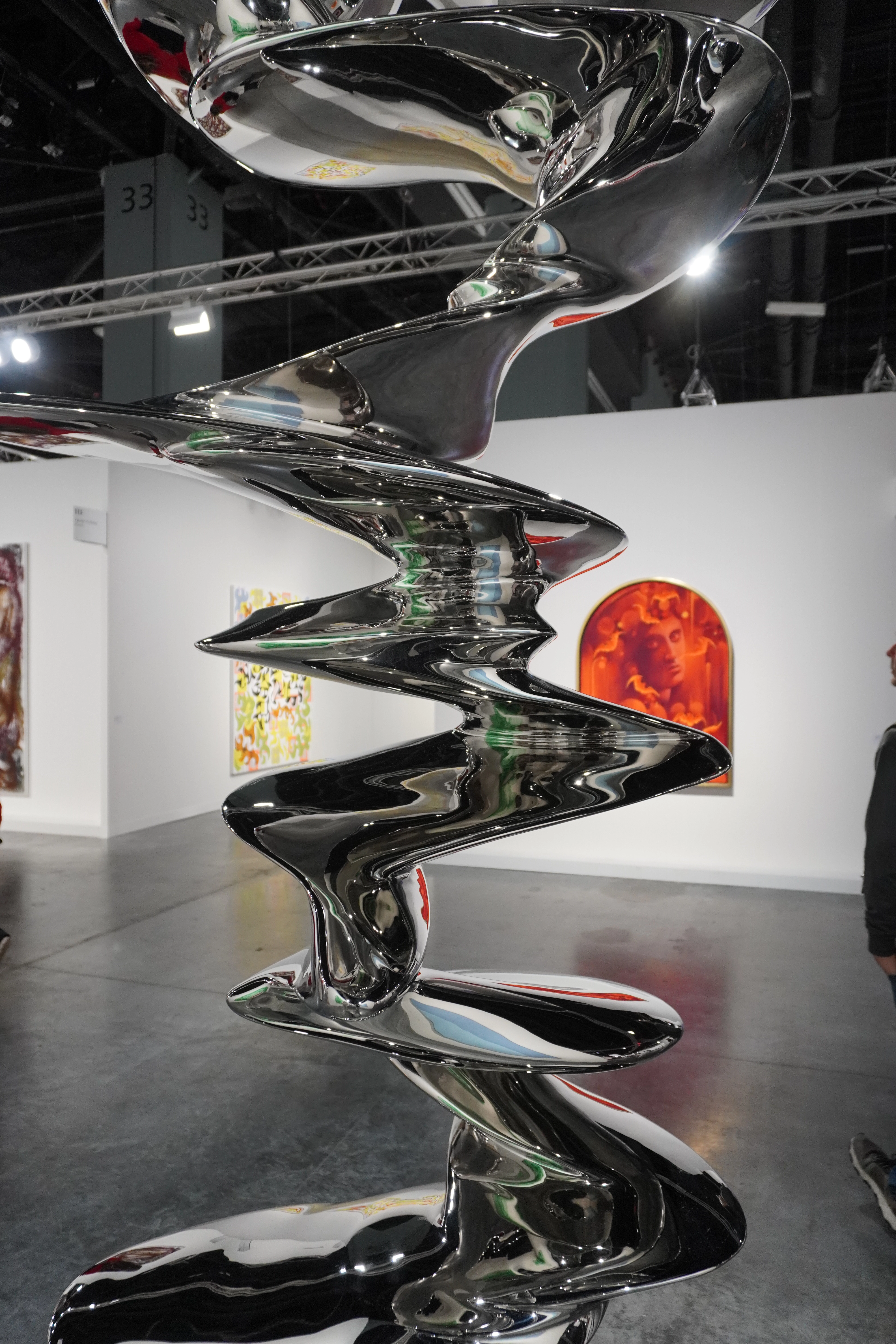 Vertical chrome sculptural installation with fluid, organic geometry in a contemporary art and design fair.