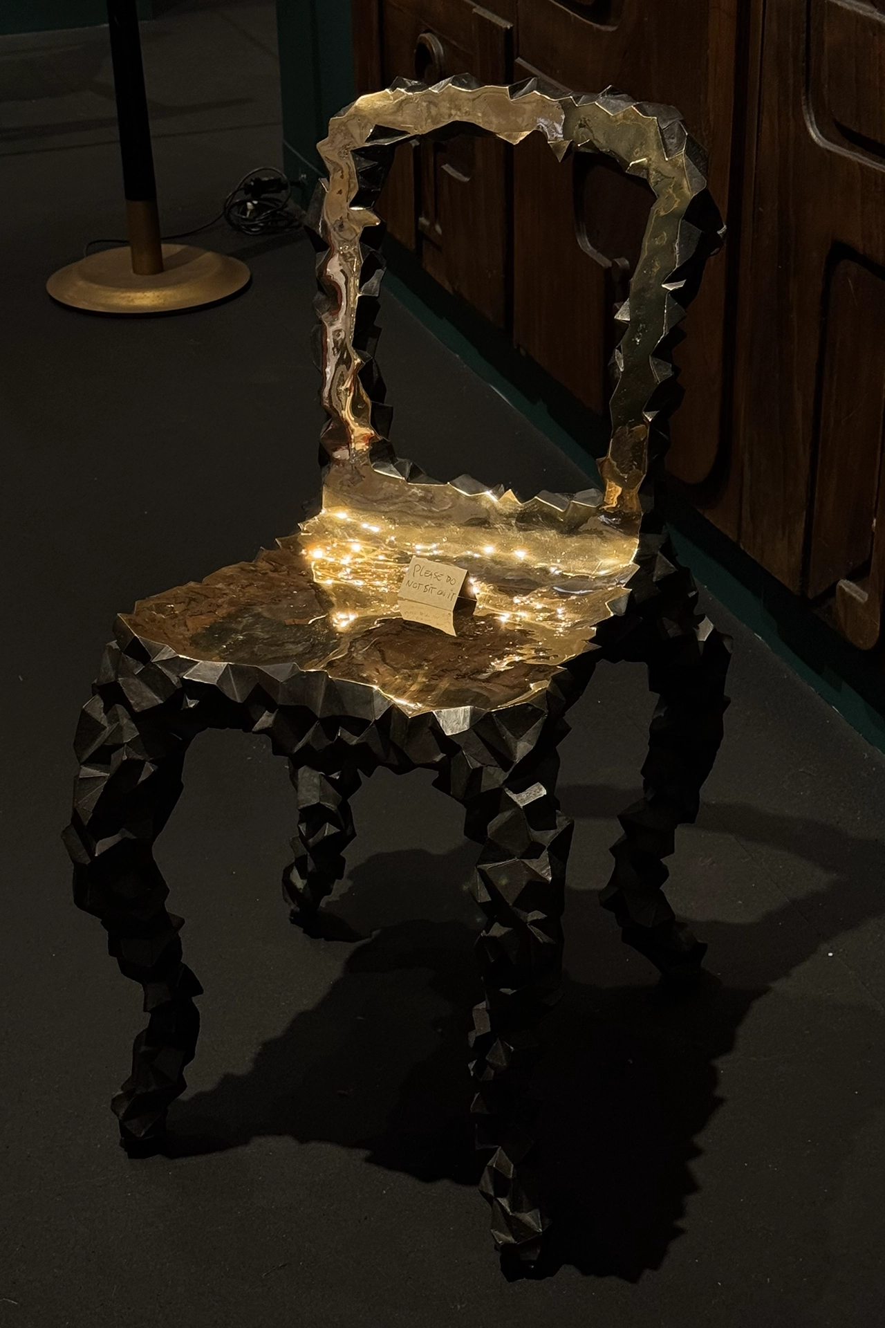 Faceted sculptural chair with metallic gold surface and angular black legs exhibited at Design Miami, representing 2026 trends in collectible design, sculptural furniture and expressive material experimentation.