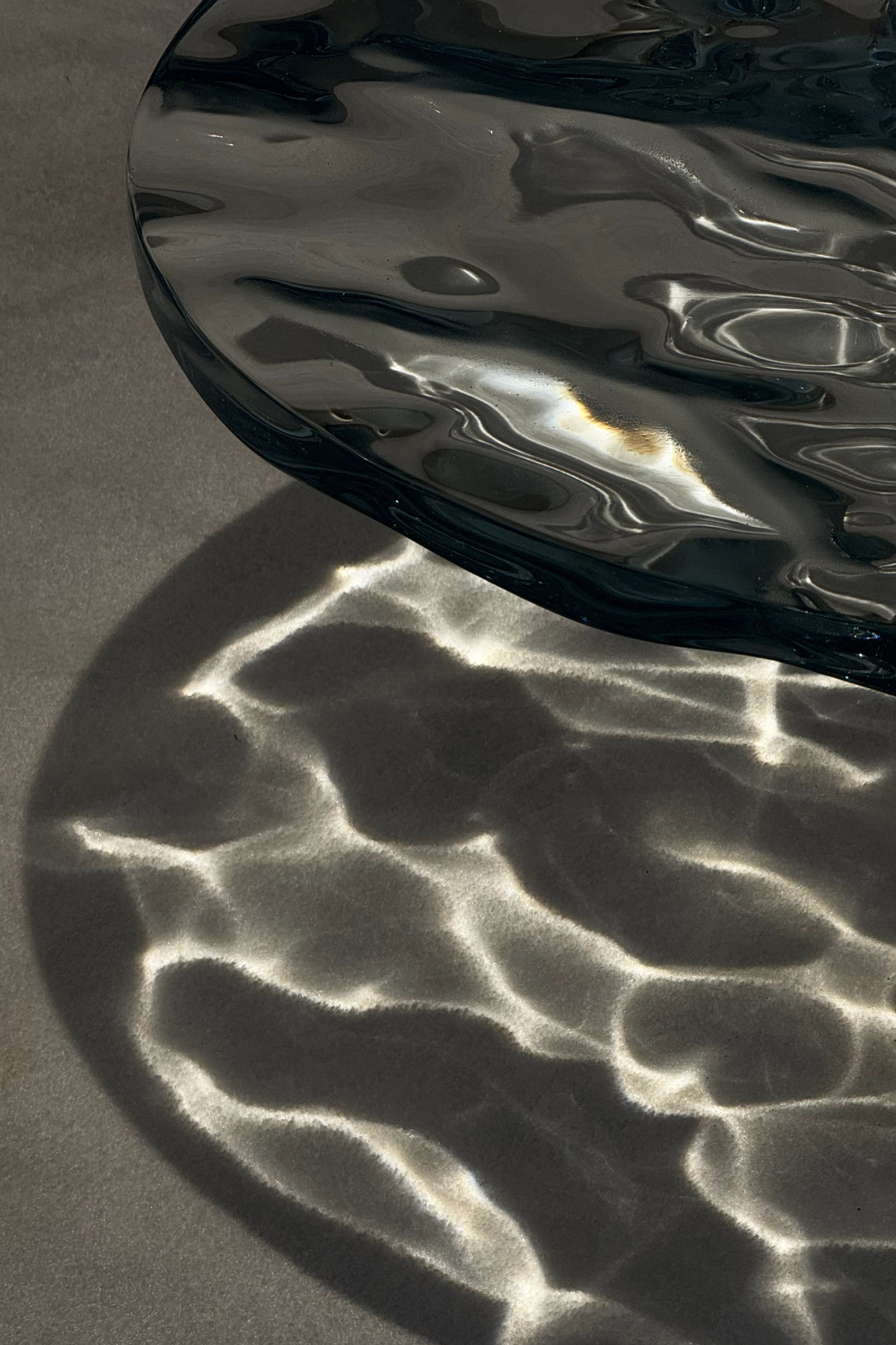 Glass sculptural object casting water-like light reflections on the floor, exploring transparency and light behavior.