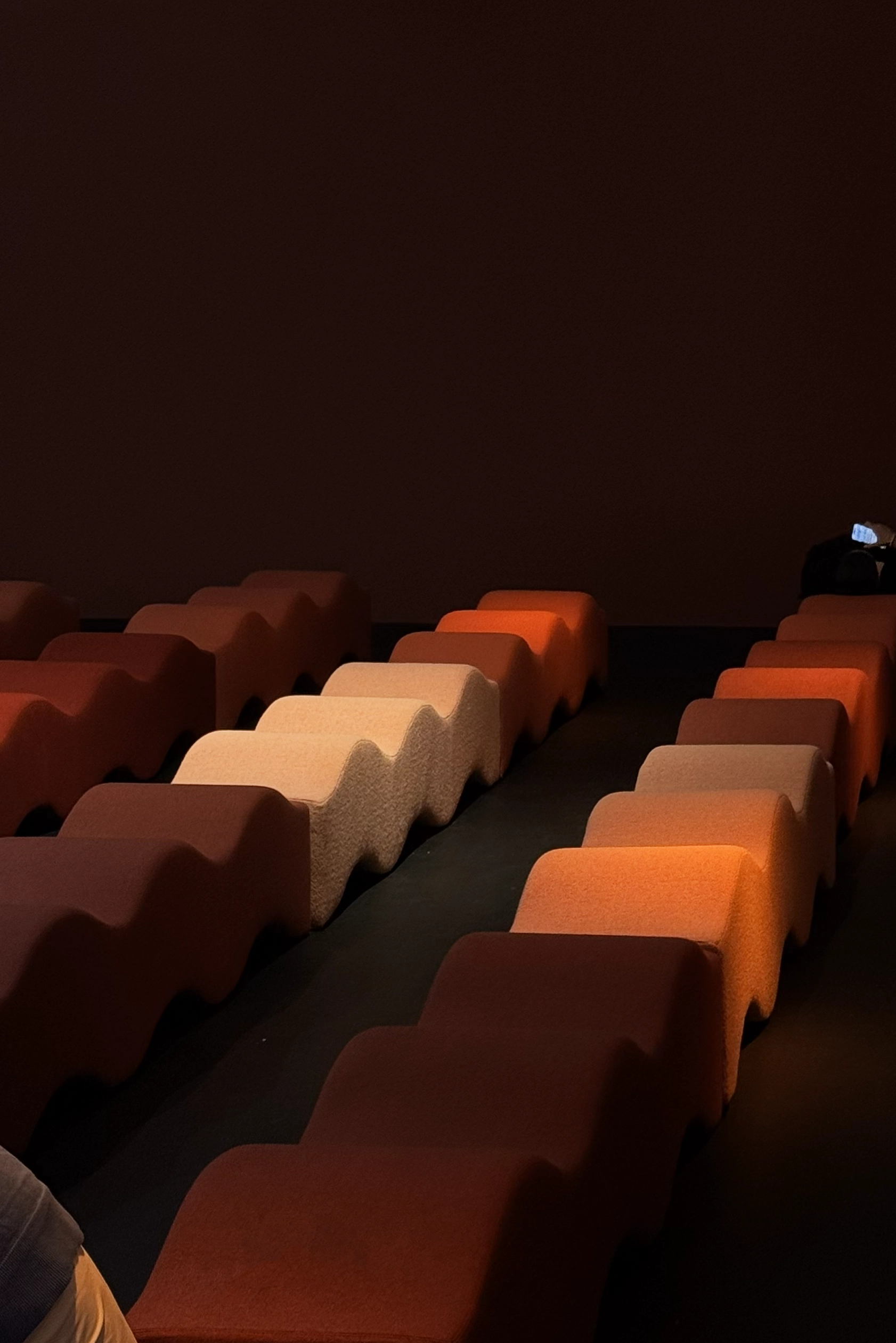 Immersive auditorium installation with upholstered seating in burgundy and oxblood tones, presented at a design exhibition.