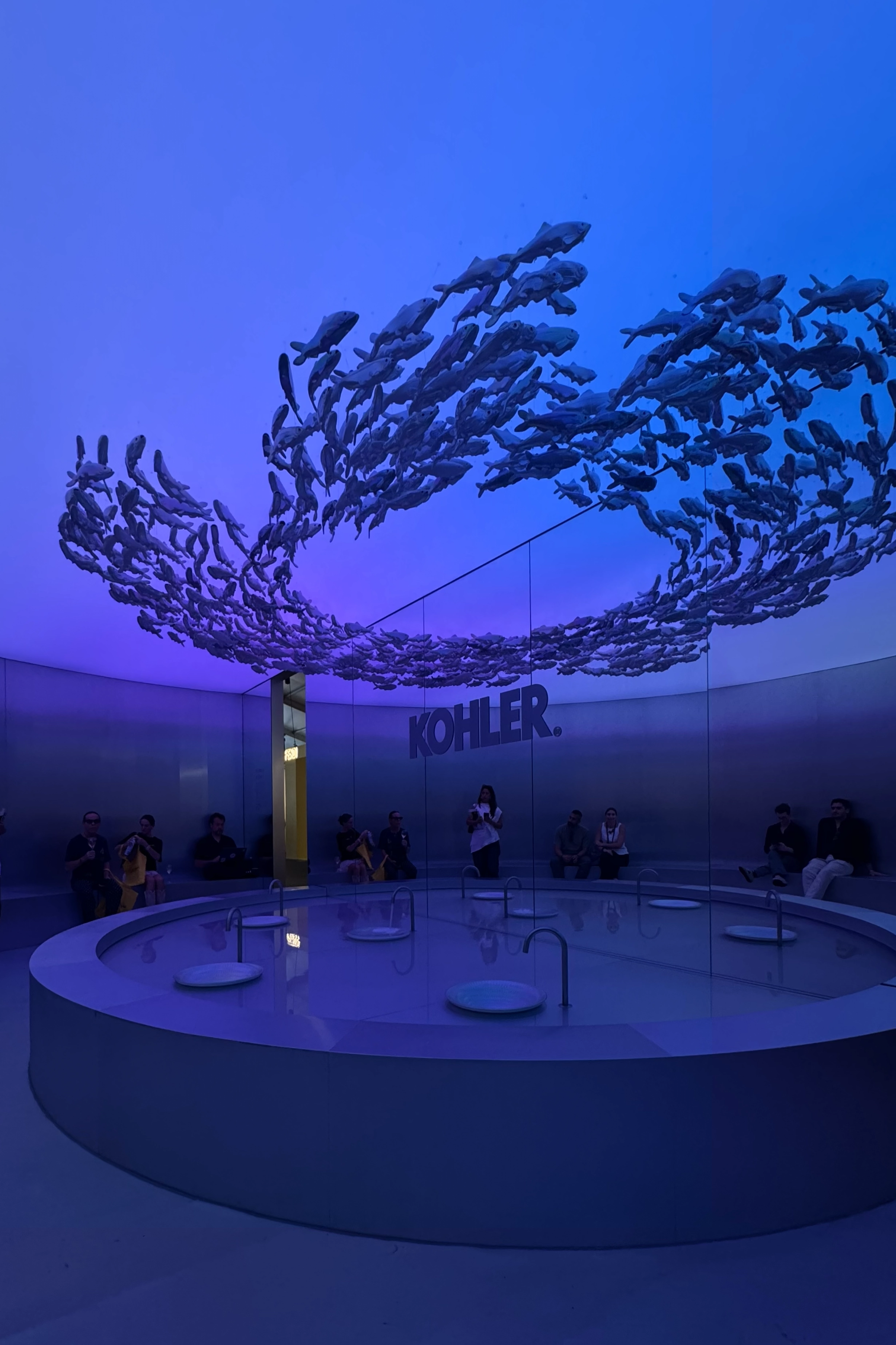 Immersive water-focused installation with circular basin, blue ambient lighting, and suspended sculptural elements at a design exhibition.
