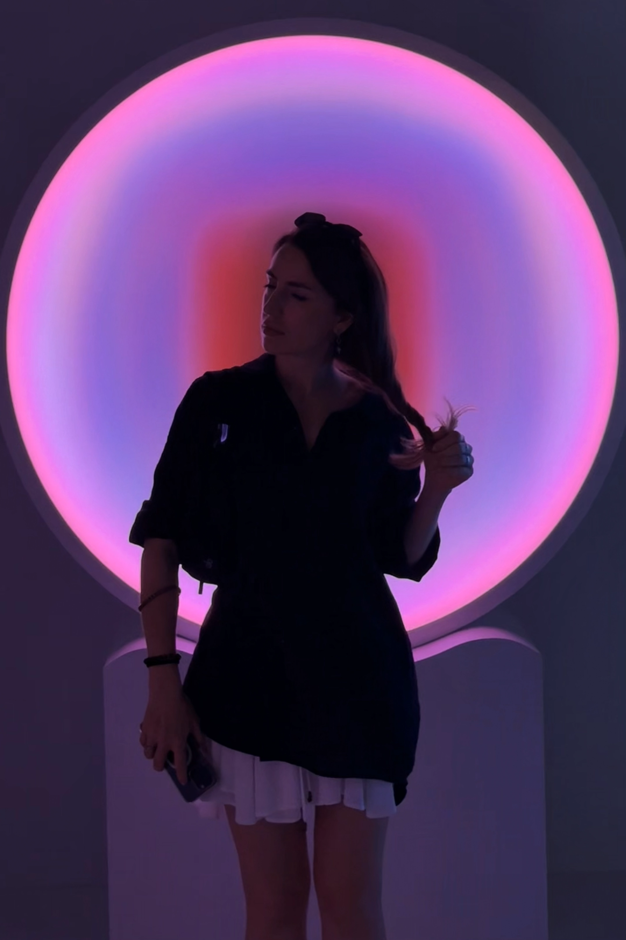 Person standing in front of a circular light installation with gradient pink and purple illumination at a design exhibition.