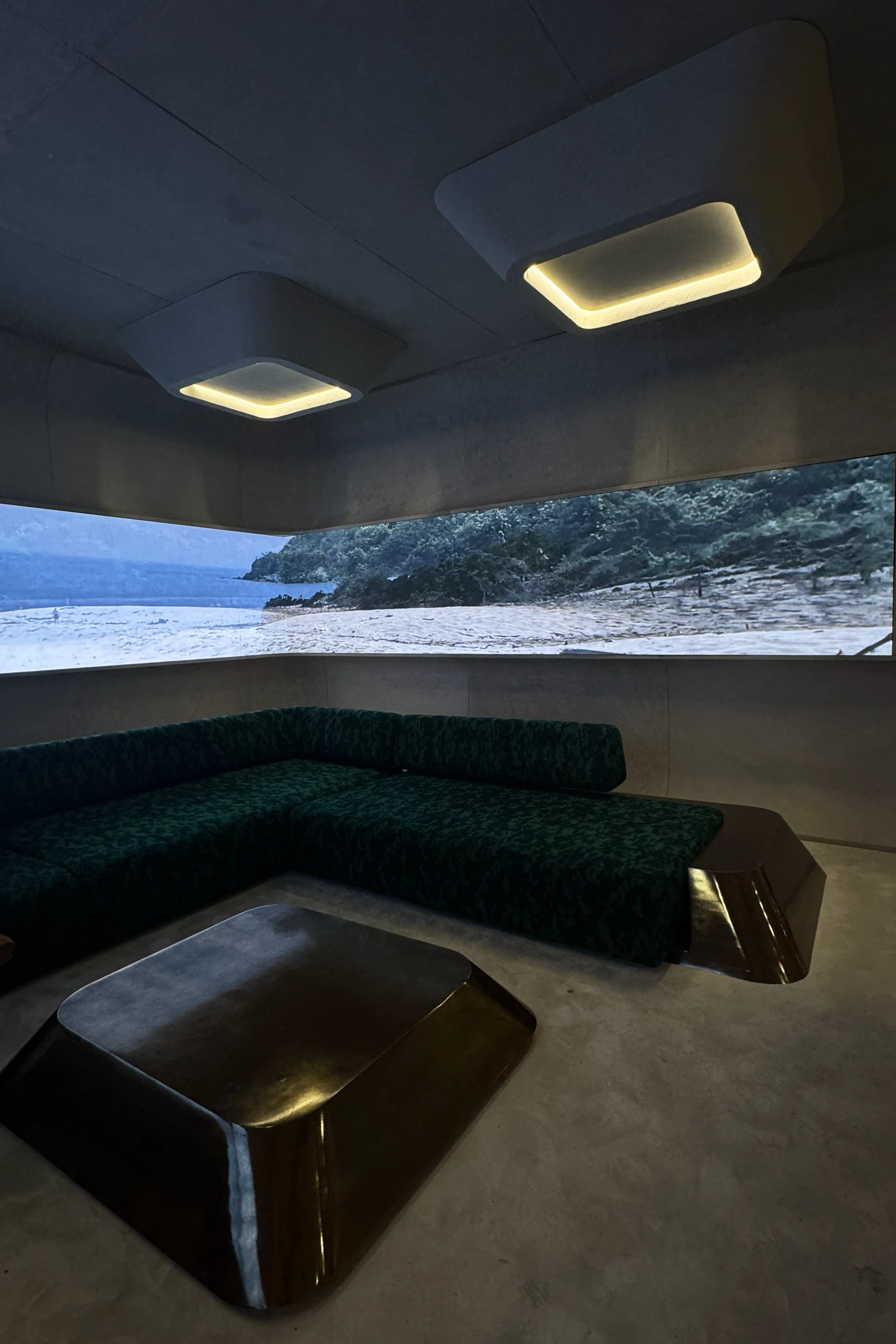 Immersive lounge installation with sculptural seating, soft architectural lighting, and panoramic landscape video display.