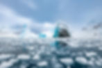 Icebergs float in a serene, icy landscape under a cloudy sky, with chunks of ice scattered on a calm blue sea, reflecting a tranquil mood.