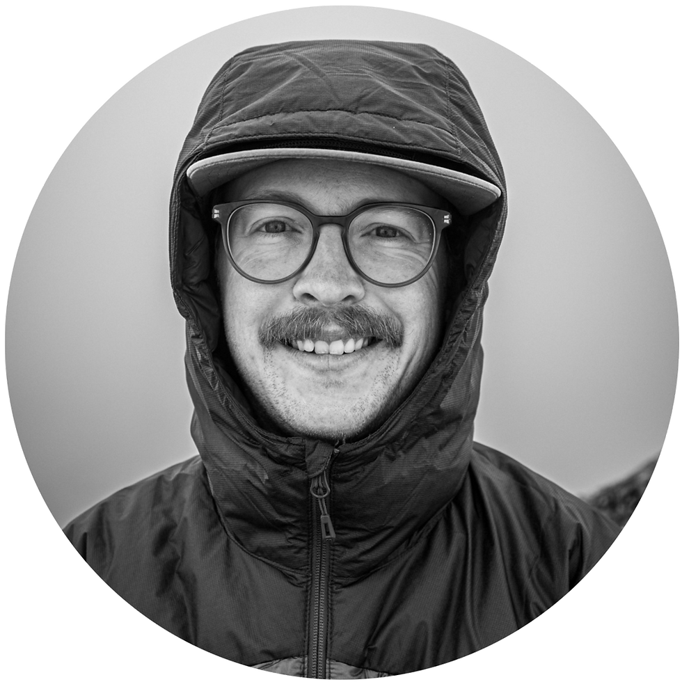 Black-and-white portrait of Keenan Hursh in glasses, hooded jacket, and cap, centered in a circular frame.