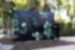 Smiling woman in black stands beside a large Outdoor MetalPrint installation of green succulents in a sunny park
