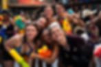 Smiling young adults at a wet foam party aim colorful water guns, with soap suds and bamboo backdrop, looking playful and excited