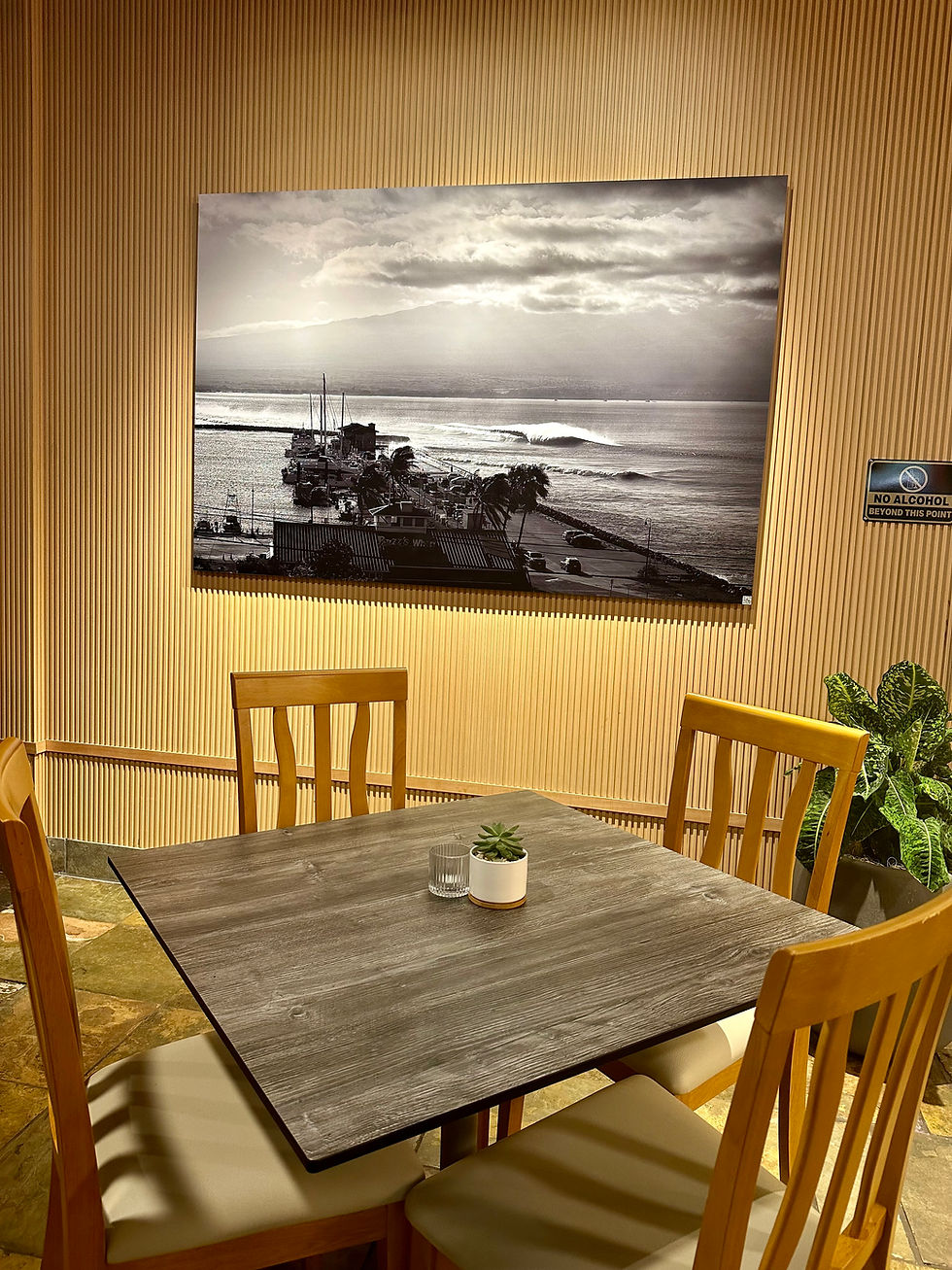 Cozy dining nook with wooden table and chairs, potted plant, coastal photo wall art, and a no alcohol beyond this point sign.