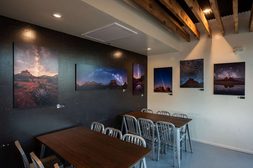 A small room with landscape photos of MetalPrints on walls, wooden tables, gray chairs. Ceiling has exposed beams; warm light creates a cozy ambiance.
