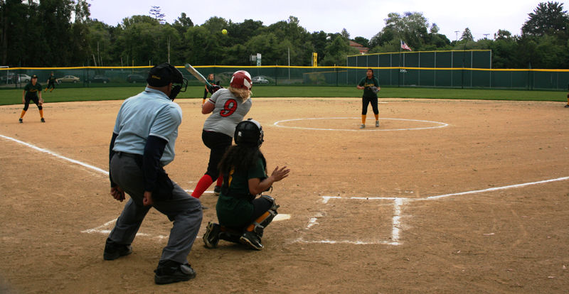 A softball game in front of a SPECTO outfield fence