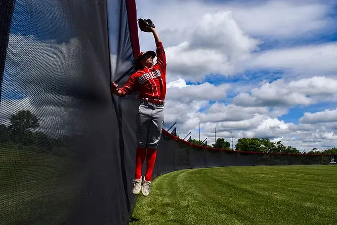 A baseball outfielder making a catch along a Specto outdoor perimeter fence