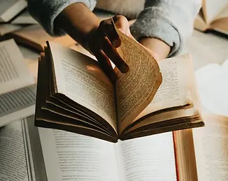 person-holds-a-book-over-a-stack-and-turns-the-page.webp