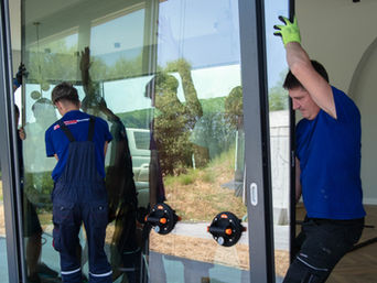 2 workers manuvering a large window glass using antive glass suction cups