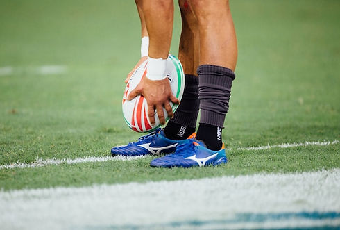 A rugby player holding a rugby ball to their feet