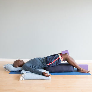 Student in Supported Bridge Pose at Three Birds Yoga Studio using supportive props.