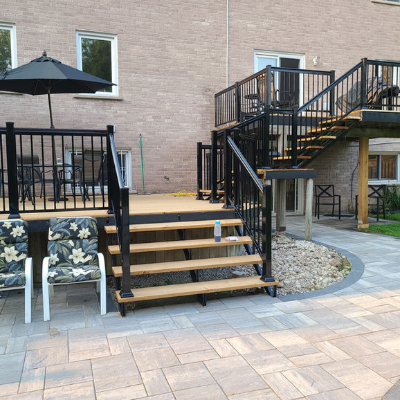 Multi-level deck with black railings, stairs, and stone patio