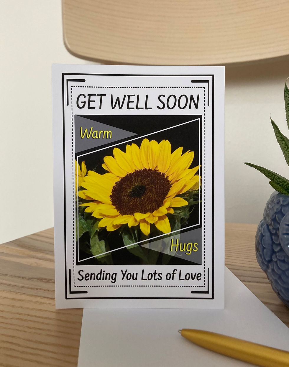 Thumbnail: Get well soon A6 greeting card next to flower pot, envelope and golden pen on the chair