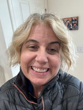 Lane (a middle age blond woman) smiles at the camera. She is wearing a riding jacket.
